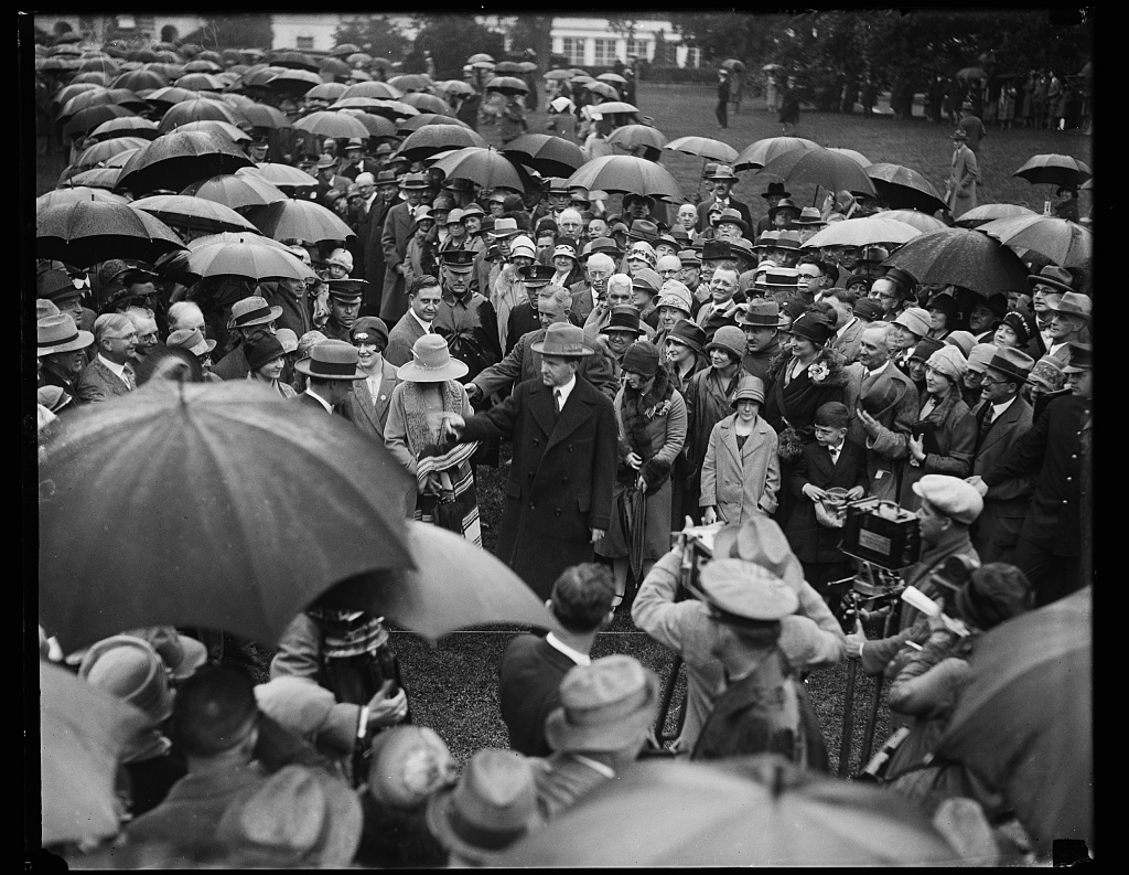 Overruling his own doctor, President Coolidge ventures out in the rain to greet the thousands of doctors gathered at the White House the day after his speech to these professionals in Washington for the American Medical Association's Annual Session, May 18, 1927. 