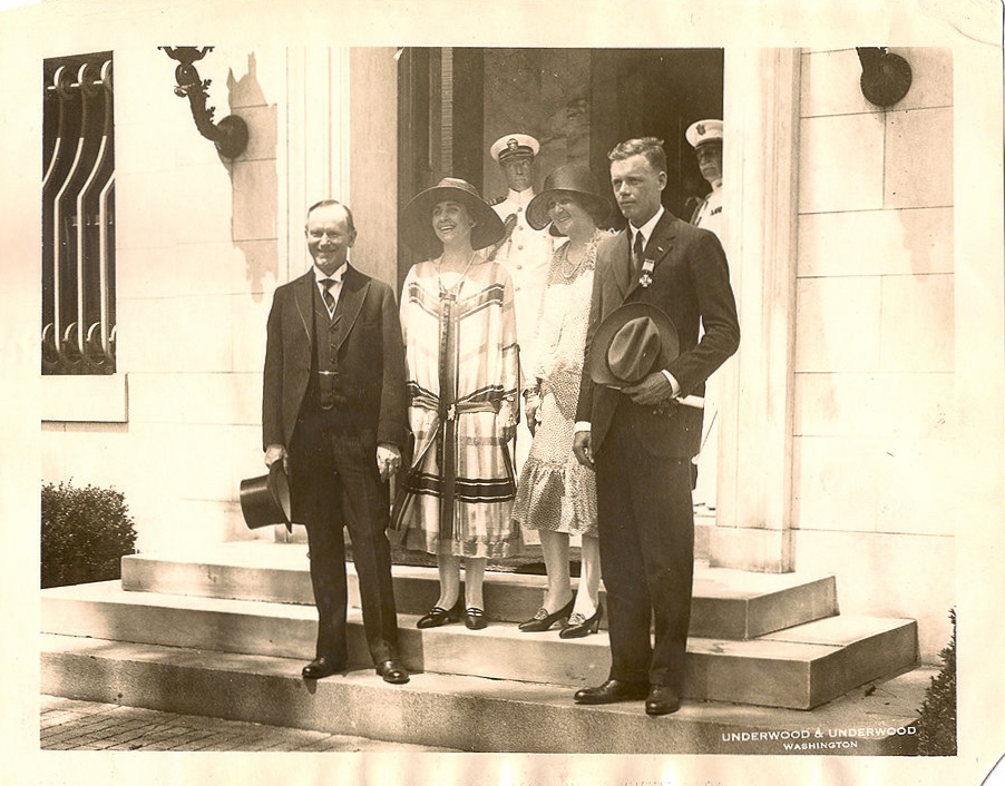 Lindbergh and his mother hosted by the Coolidges at DuPont Circle, where the President and his wife stayed during repairs to the White House roof that spring. Notice how everyone is cheerful except the unexpectedly sober figure on the right. Lindbergh, about to appear in a light suit, was corrected by Coolidge who chose a dark suit for him as better befitting the formality of the occasion. Even returning heroes need to take care of the way they dress. They set a deeper example than they may realize, one  that should not be treated flippantly. 