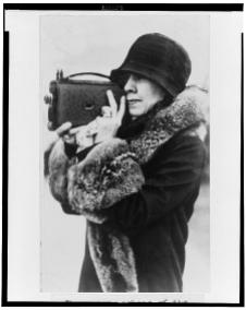 Mrs. Coolidge, member of the White House News Photographers Association, half-length portrait, standing, facing left, holding camera up to face 2-9-1929